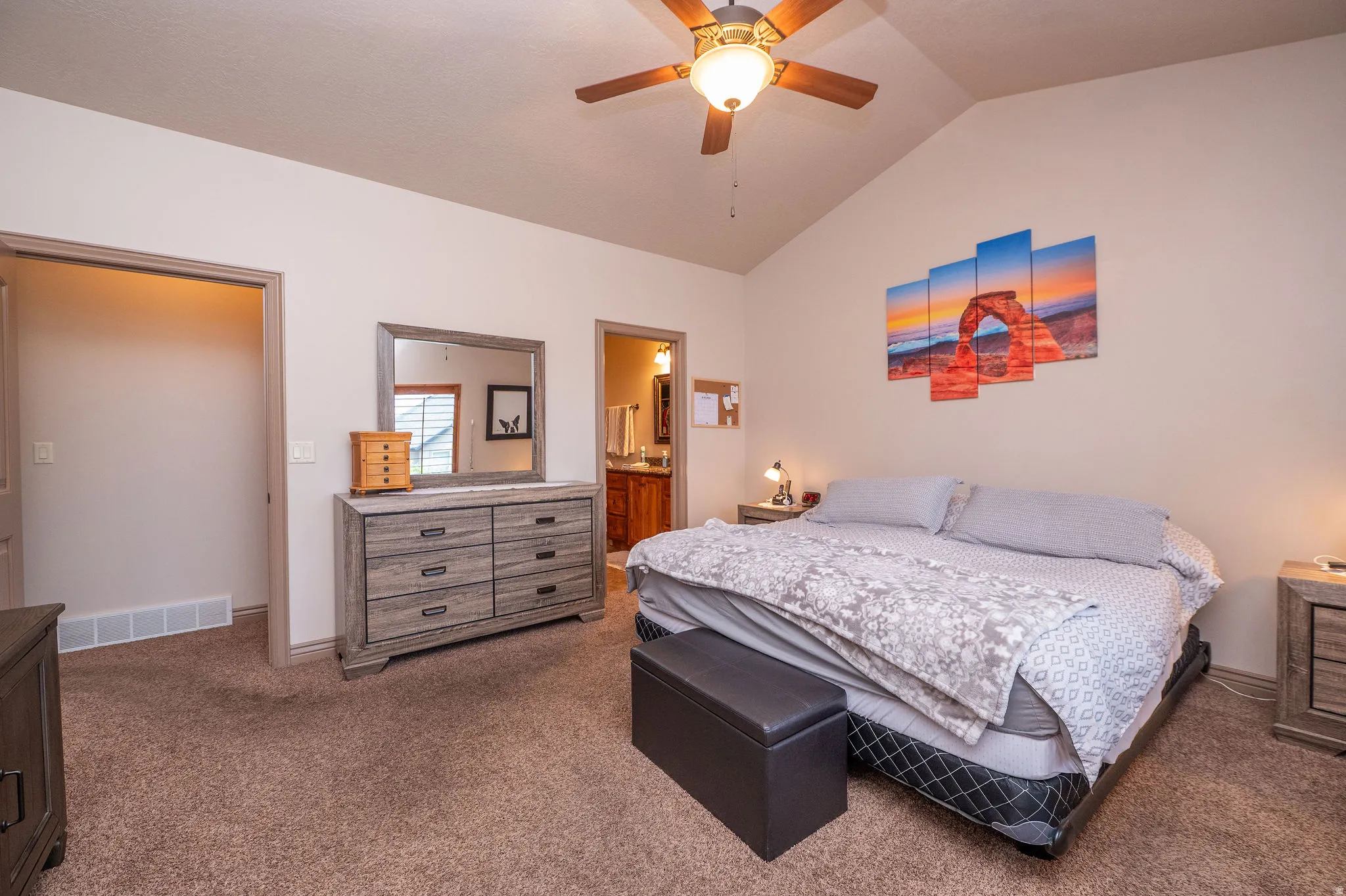 Second angle of the primary suite reveals the walk-in closet entry and ensuite bathroom beyond. Vaulted ceilings add that extra touch of luxury.
