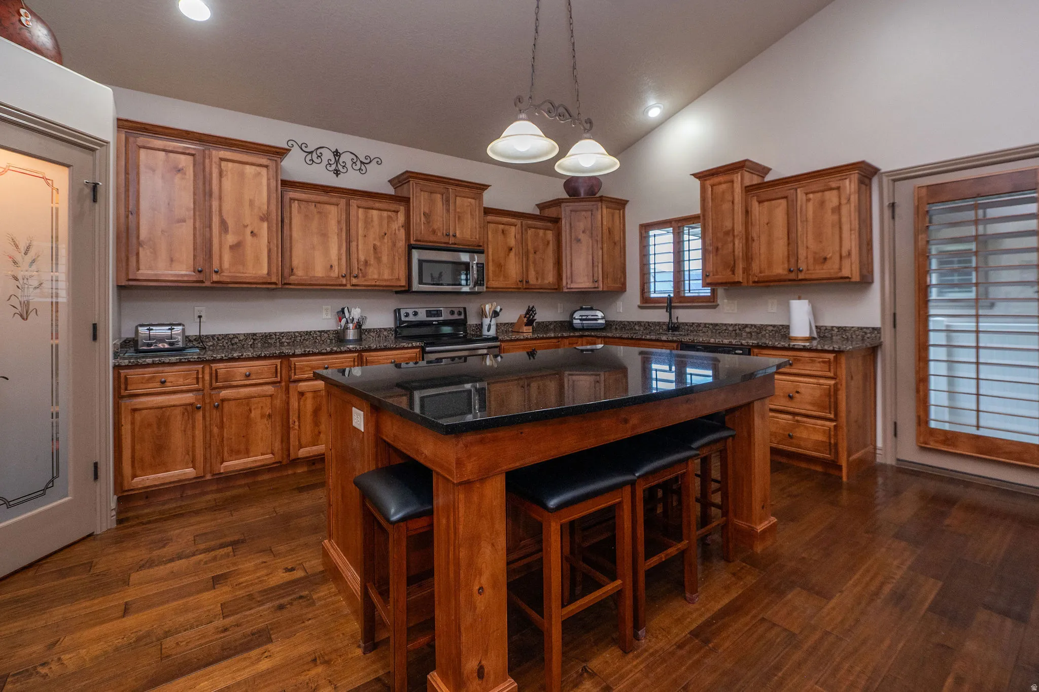Another gorgeous look at this kitchen, showcasing the full run of knotty alder cabinetry, granite countertops, stainless appliances, hardwood floors, and that bold black granite island. The etched glass pantry door is a standout detail.