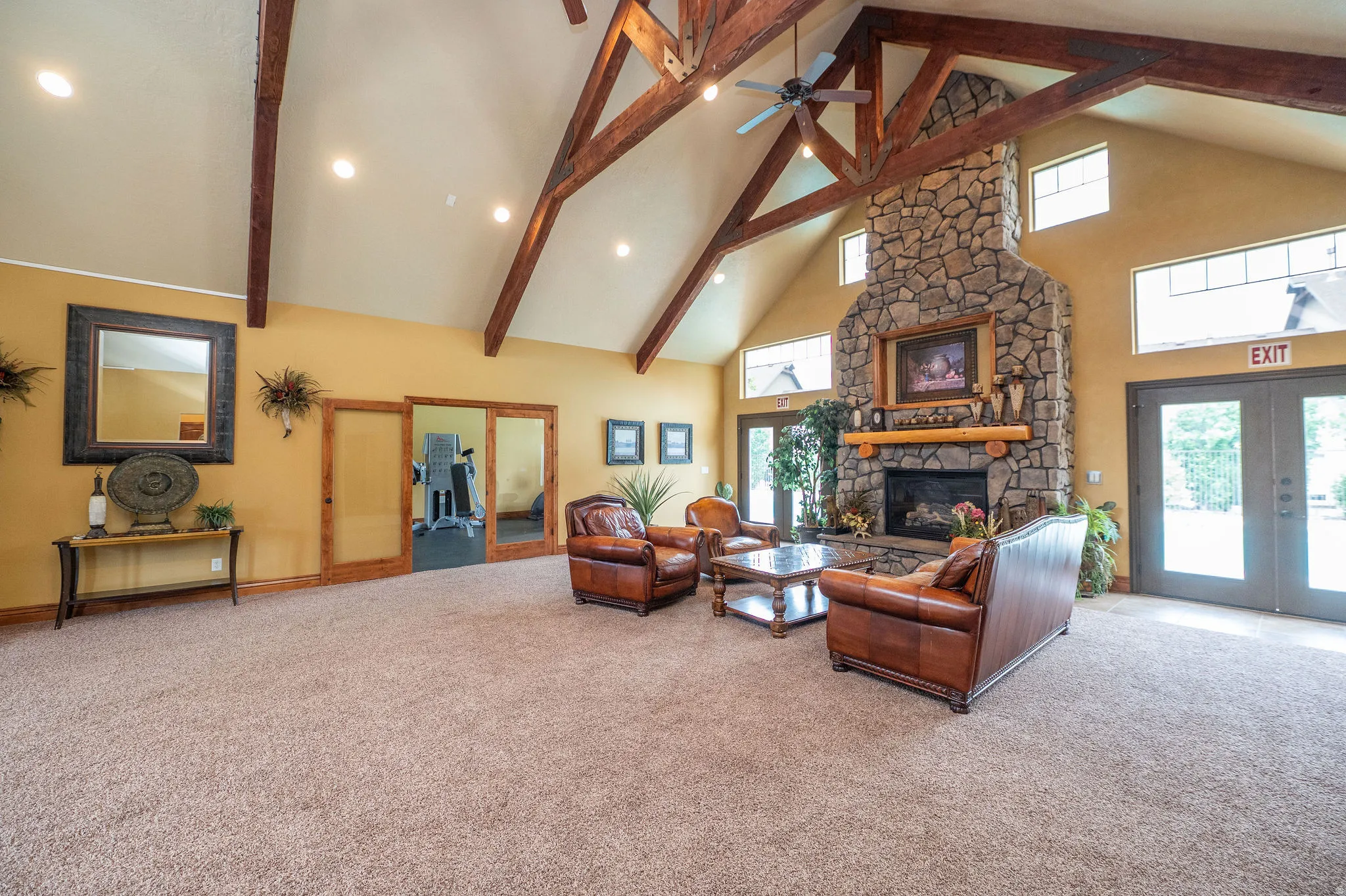 Full wide angle of the clubhouse great room reveals the true scale of this impressive space. Soaring exposed beam vaulted ceilings, stone fireplace, leather seating, and direct access to both the fitness room and pool patio. This is a serious amenity.