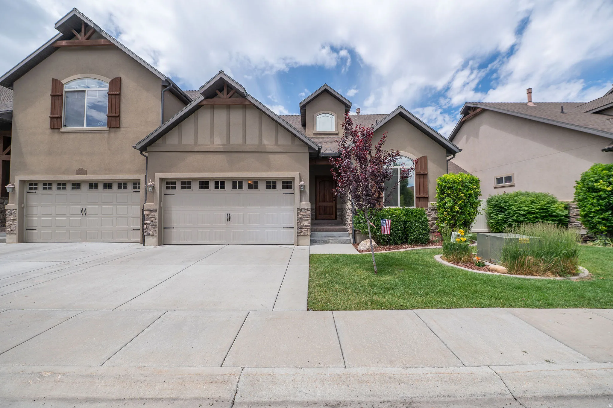 Beautiful daytime curb appeal showcasing craftsman-style architecture, 2-car garage, stacked stone accents, board-and-batten details, ornamental tree, and lush manicured landscaping.