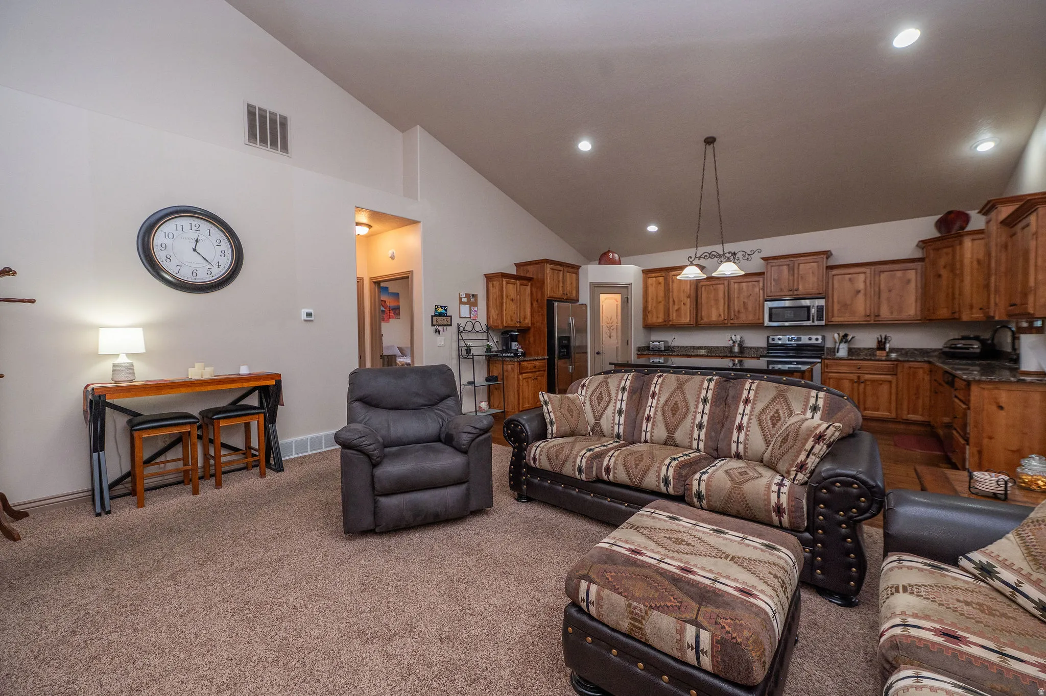 Open-concept living and kitchen space with vaulted ceilings, recessed lighting, and a seamless flow between rooms. Knotty alder cabinetry and granite counters visible from here set the tone for what the kitchen delivers.