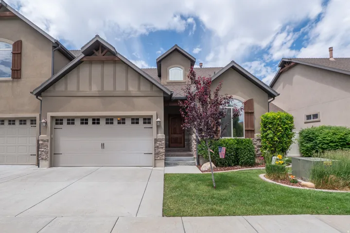 Closer look at the front entry, highlighting the warm wood front door, arched windows, stacked stone columns, and thoughtfully planted flower beds. Solid, stunning craftsmanship from the street.