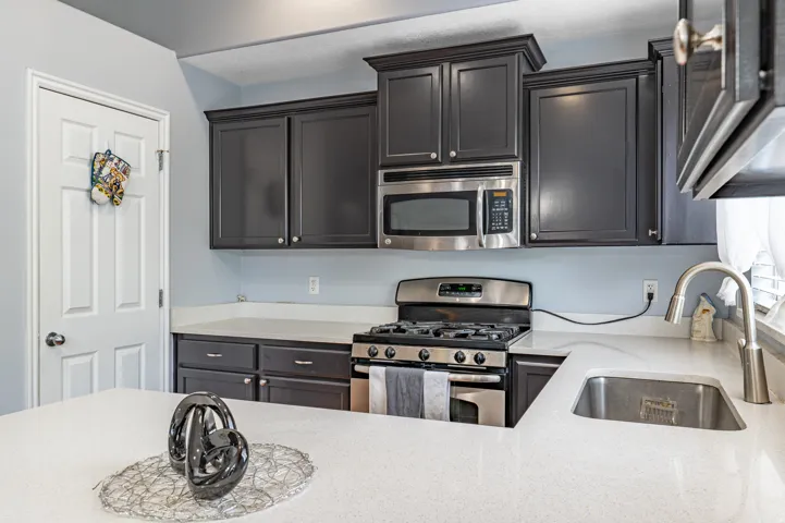 Kitchen featuring dark cabinetry, stainless steel appliances, a gas range, and light-toned countertops