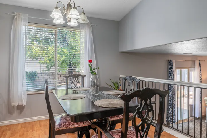 Dining area featuring wood-finish flooring, a contemporary chandelier, and a large window with blinds and sheer curtains