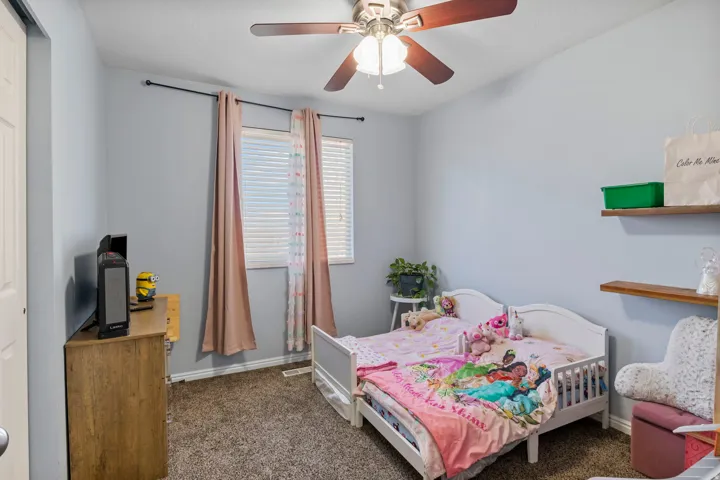 Bedroom featuring light gray walls, carpeted flooring, two windows with blinds, and a ceiling fan with light fixture