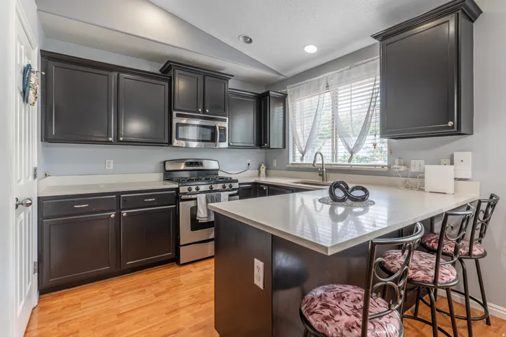 Kitchen featuring dark cabinetry, stainless steel appliances, light-toned countertops, wood-finish flooring, and a breakfast bar
