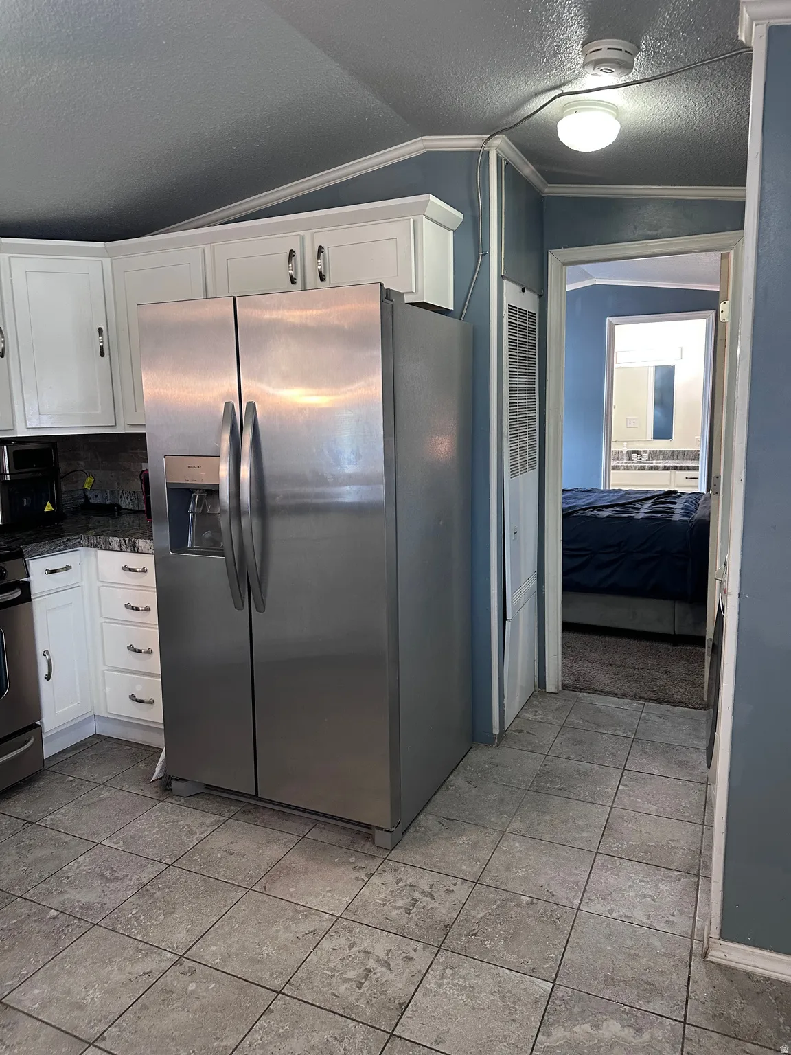 Kitchen featuring a stainless steel side-by-side refrigerator, white cabinetry, dark countertops, and square tile flooring