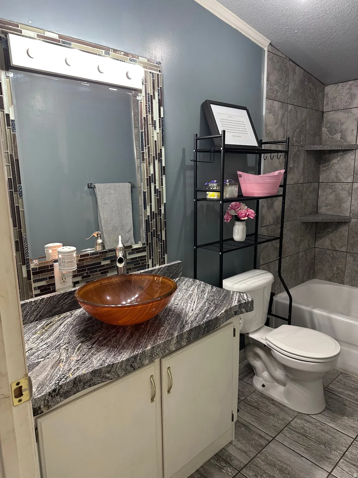 Bathroom featuring a vessel sink with a silver-tone faucet, a vanity with a patterned countertop, and light-toned cabinetry