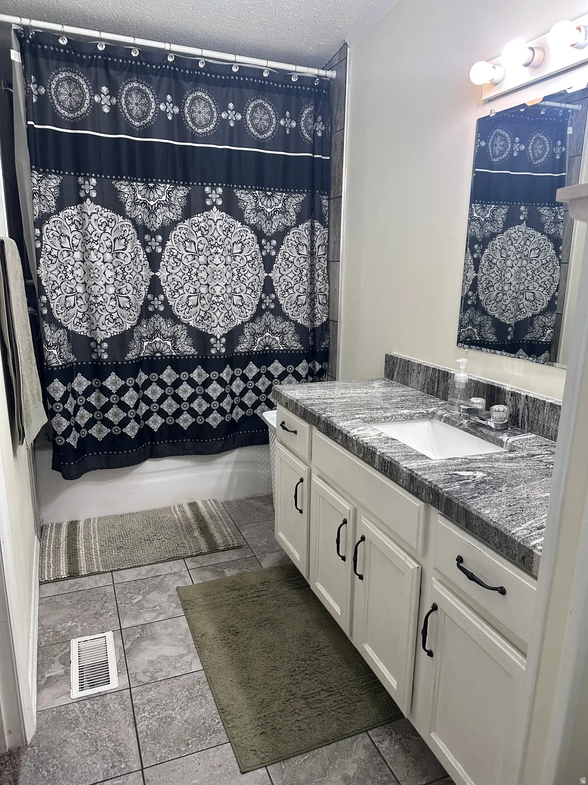 Bathroom featuring a white vanity with panel-front cabinetry, dark hardware, and a granite-finish countertop with an undermount sink