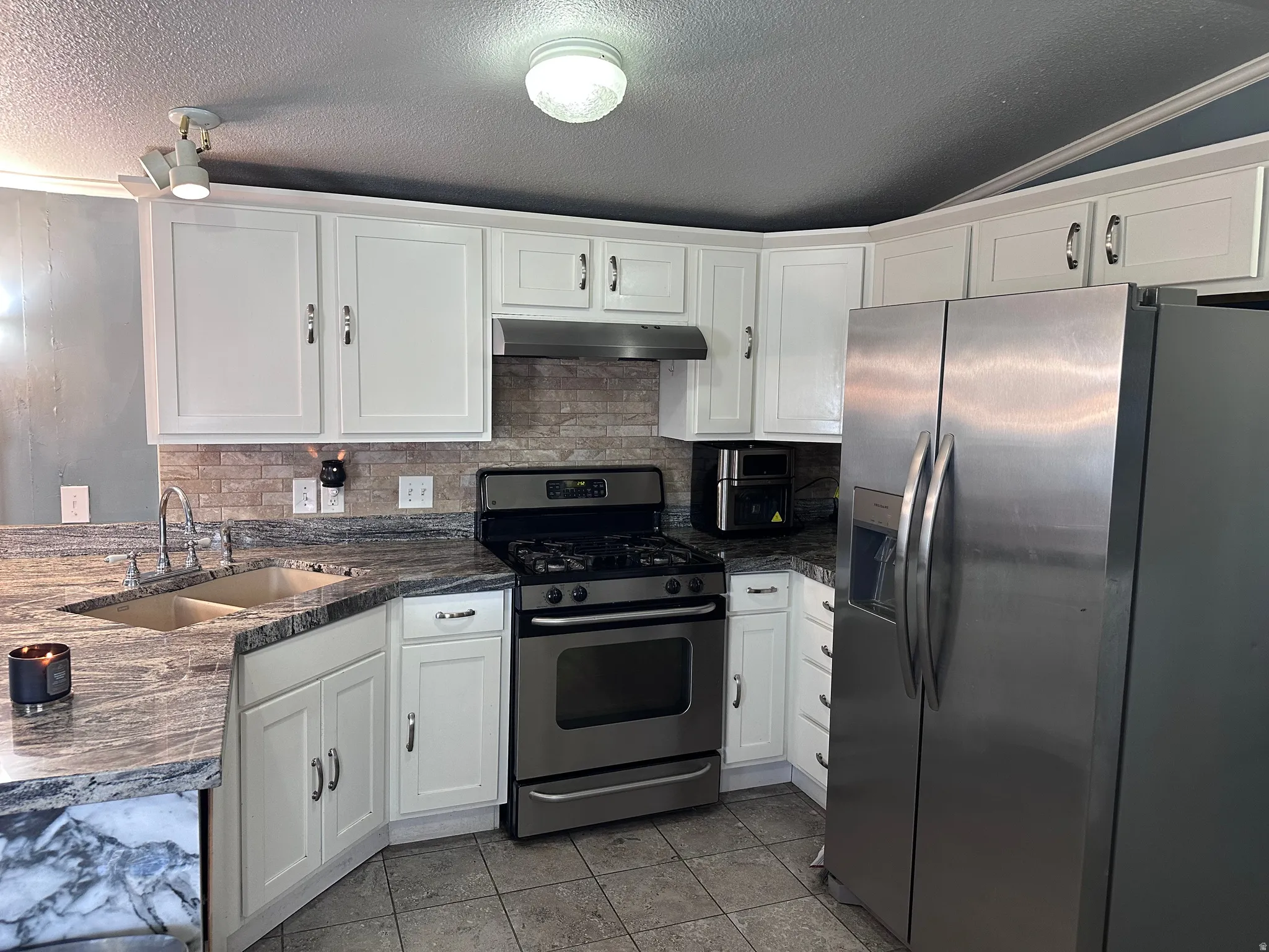 Kitchen featuring white cabinetry, stone countertops, a tile backsplash, stainless steel appliances, and tile flooring