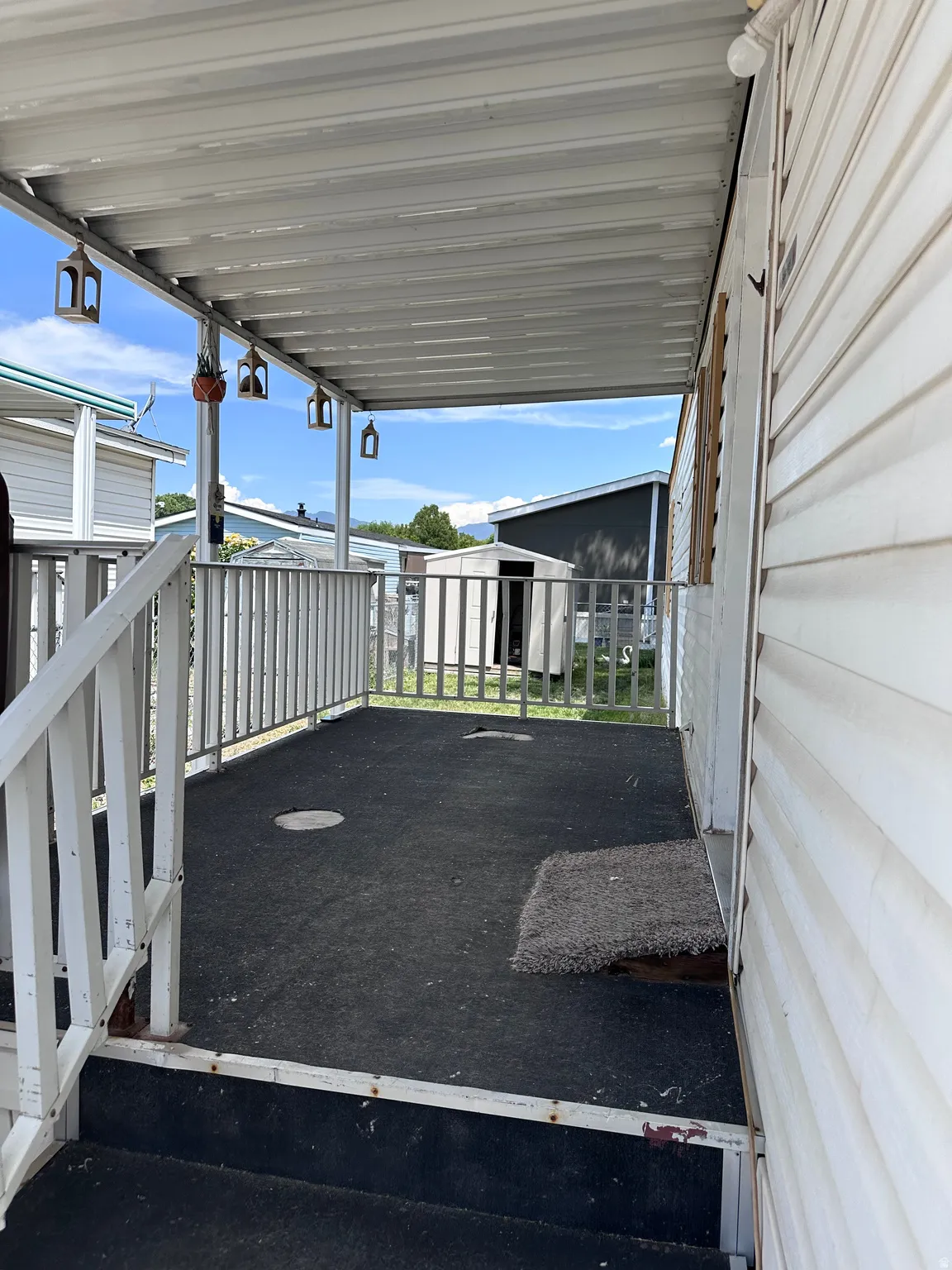 Covered exterior porch featuring white railing, dark-toned flooring, and a white corrugated roof
