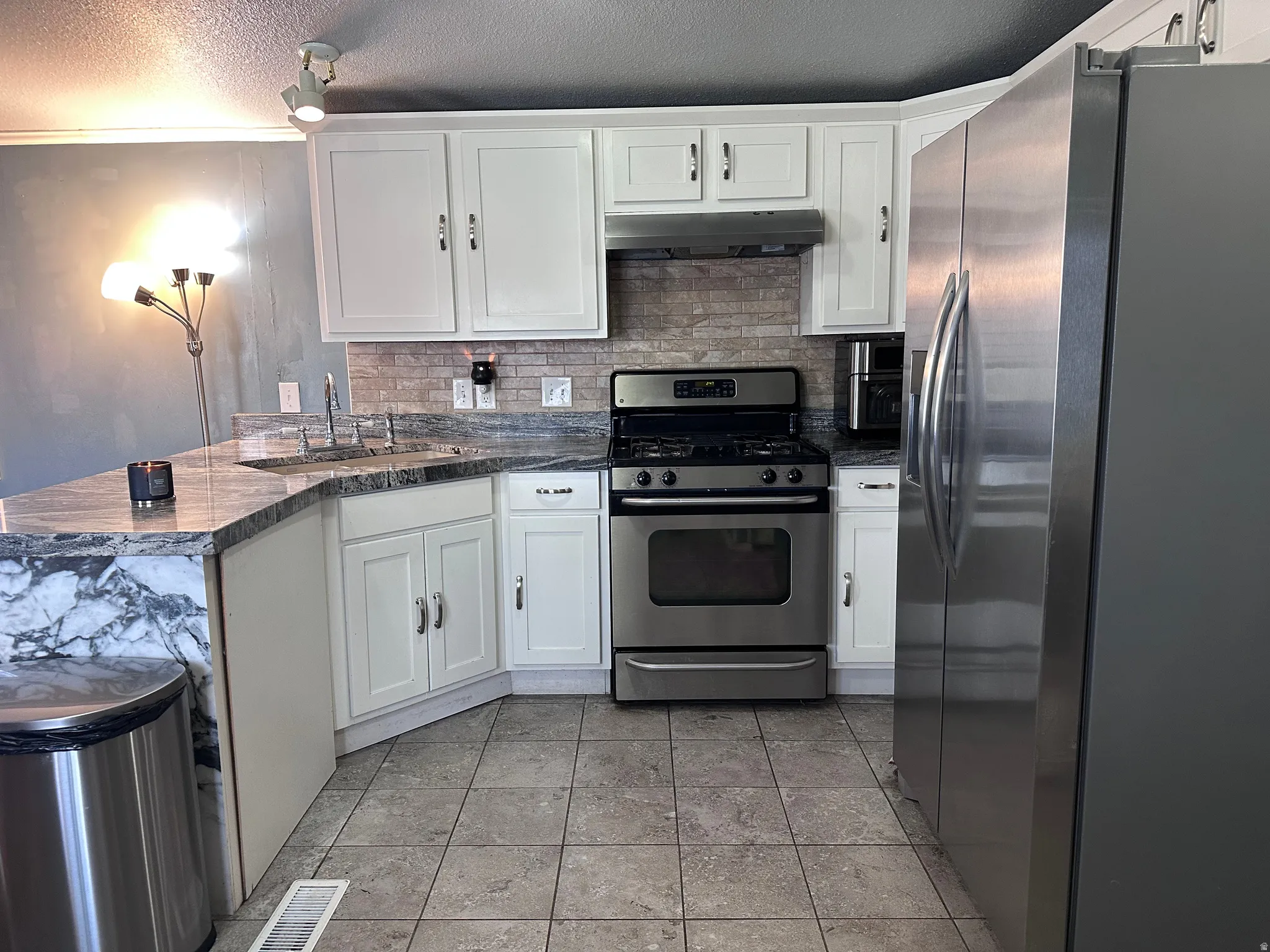 Kitchen featuring white cabinetry, stone countertops, stainless steel appliances, tile flooring, and a subway tile backsplash