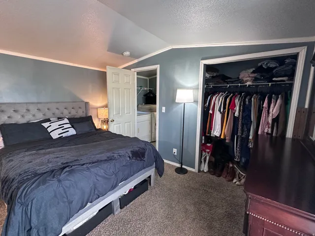 Carpeted room featuring a tufted headboard, angled wall, built-in closet with shelving and hanging rod, and white trim