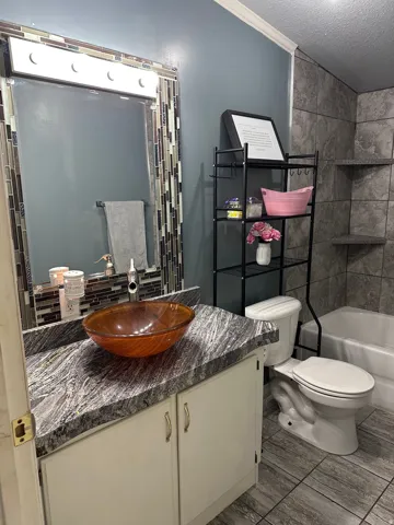 Bathroom featuring a vessel sink with a silver-tone faucet, a vanity with a patterned countertop, and light-toned cabinetry