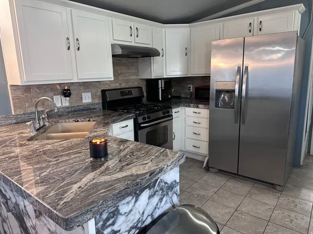 Updated kitchen featuring white shaker cabinetry, patterned stone countertops, stainless steel appliances, a tile backsplash, and tile flooring