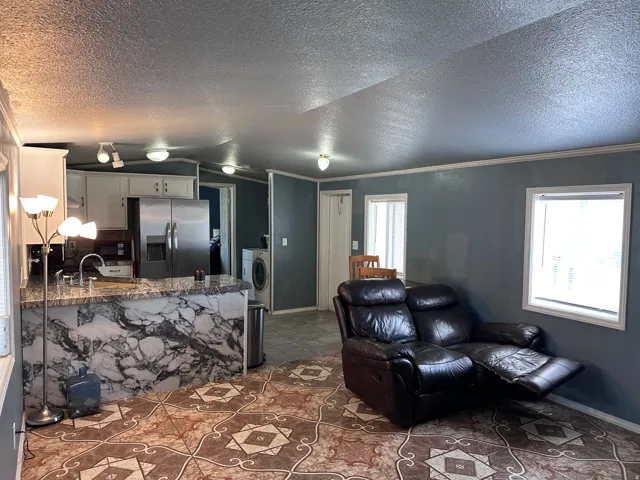 Kitchen and living area featuring patterned tile flooring, an eat-at kitchen island with a marbled finish, white cabinetry, and stainless steel appliances