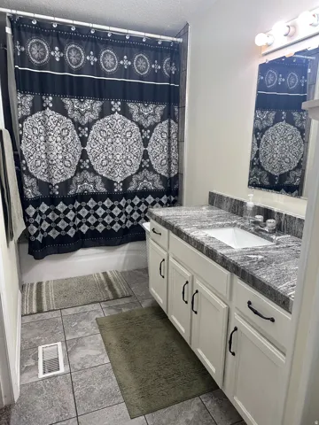 Bathroom featuring a white vanity with panel-front cabinetry, dark hardware, and a granite-finish countertop with an undermount sink