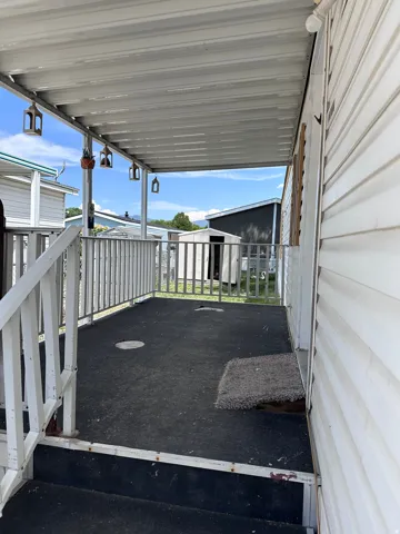 Covered exterior porch featuring white railing, dark-toned flooring, and a white corrugated roof