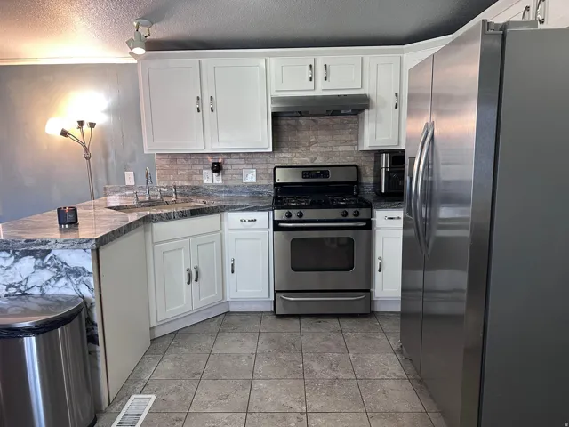 Kitchen featuring white cabinetry, stone countertops, stainless steel appliances, tile flooring, and a subway tile backsplash