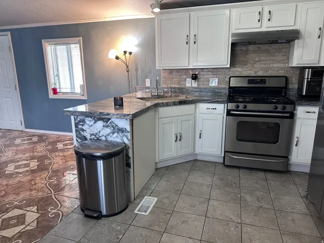 Kitchen featuring white cabinetry with brushed nickel hardware, stainless steel gas range, and a tile backsplash