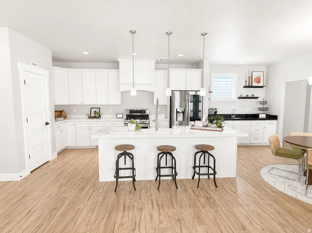 Modern kitchen with soft close white cabinetry, a large center island with farm sink, stainless steel LG ThinQ appliances, and light wood-finish flooring.