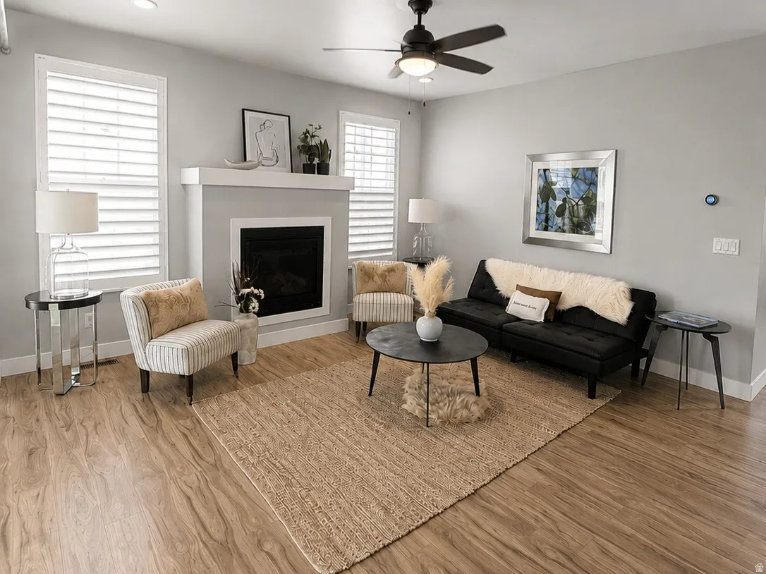 Living area featuring wood-finish flooring, a fireplace with a white mantel, and a ceiling fan