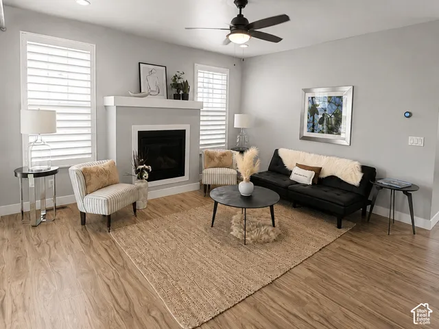 Living area featuring wood-finish flooring, a fireplace with a white mantel, and a ceiling fan