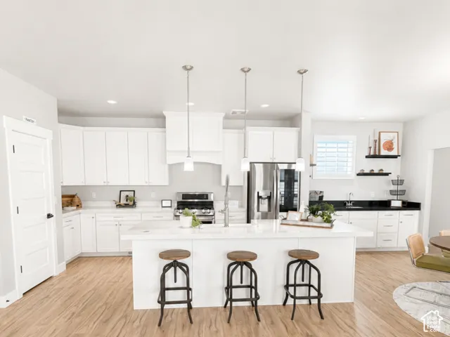 Kitchen with white cabinetry, stainless steel appliances, a large island with pendant lighting, and wood-finish flooring