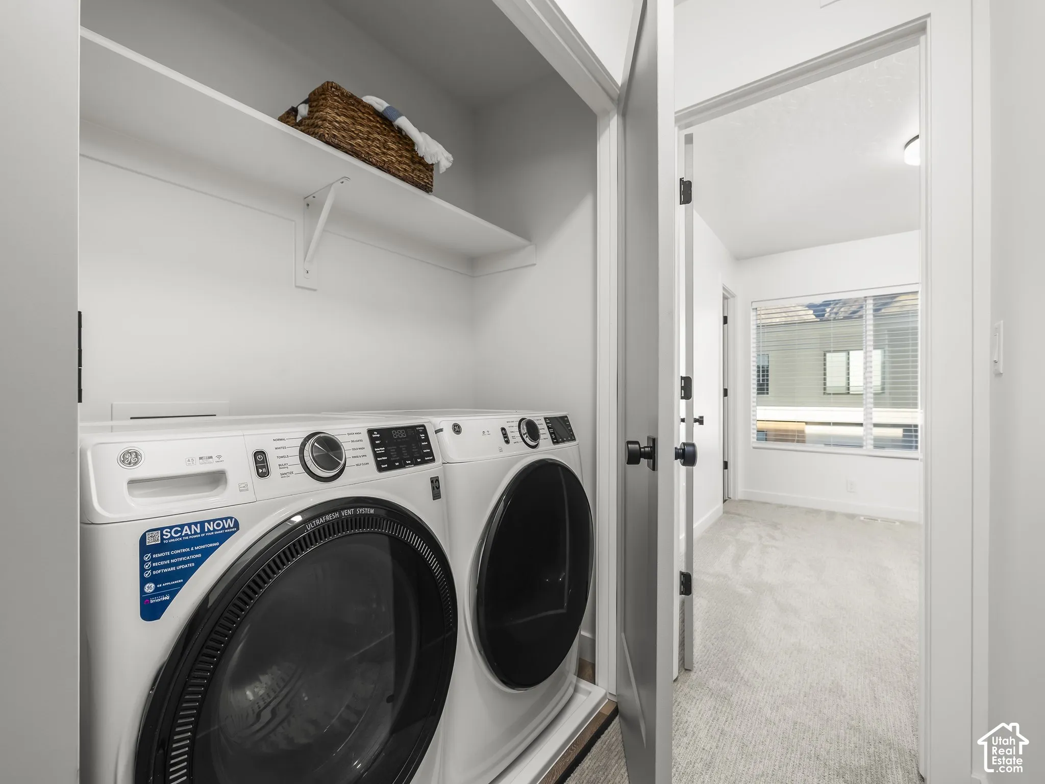 Dedicated laundry area featuring a white front-load washer and dryer set, an overhead storage shelf, and light wall finishes