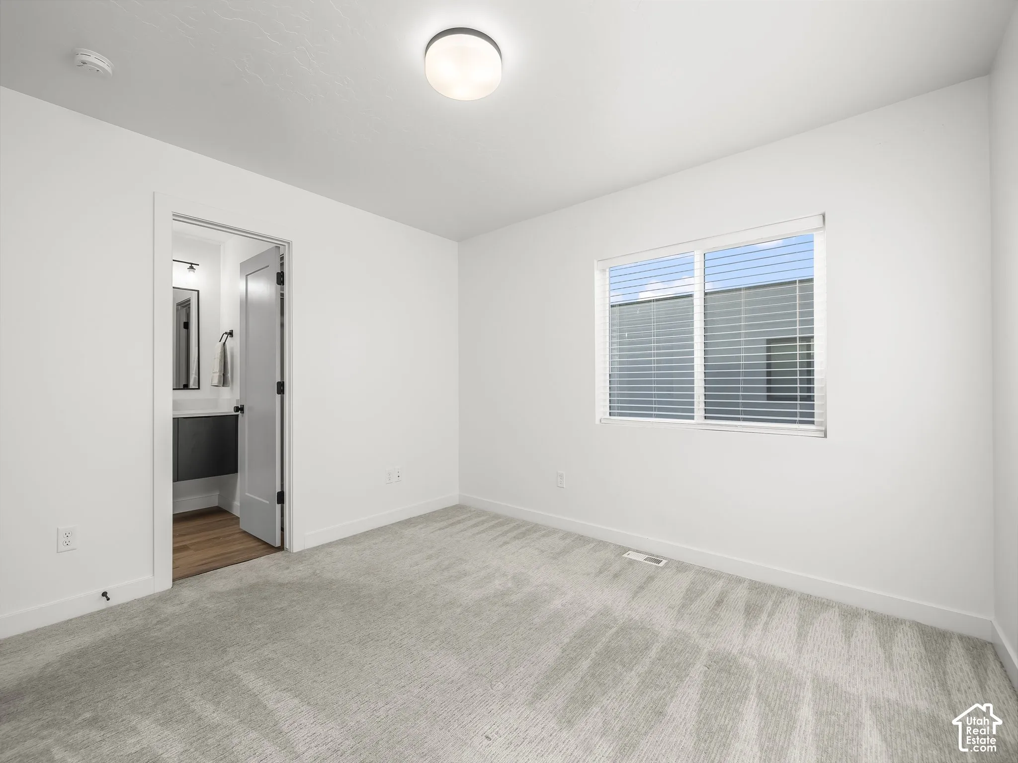 Carpeted room with white walls, a single window with blinds, and an overhead flush-mount light fixture