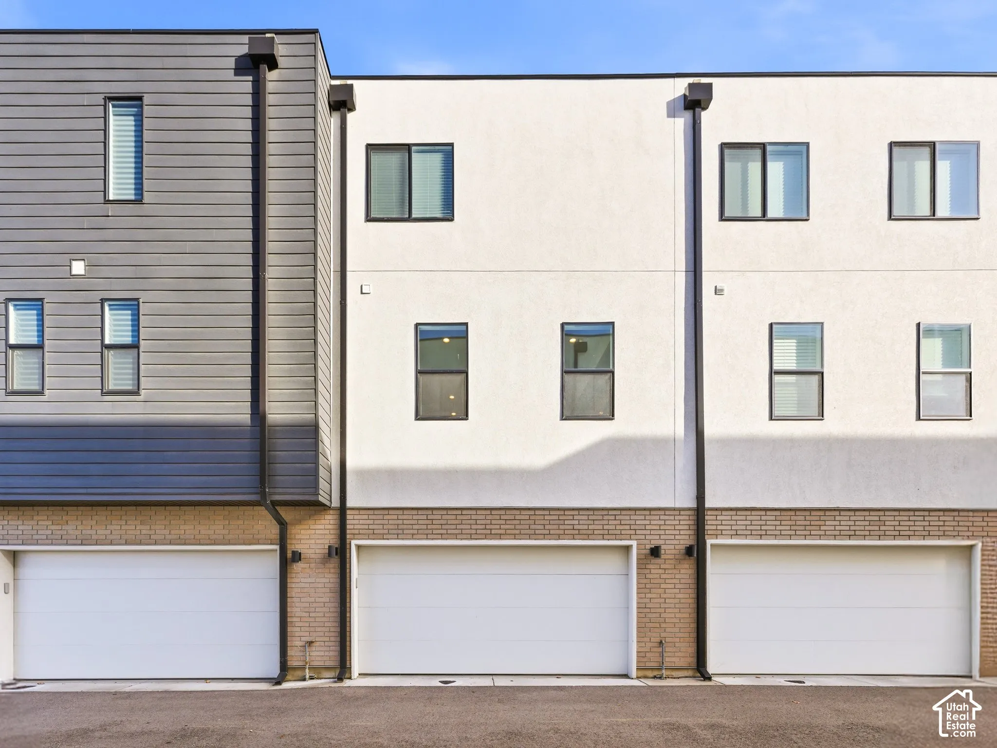 Modern multi-story facade featuring three attached garages with white doors