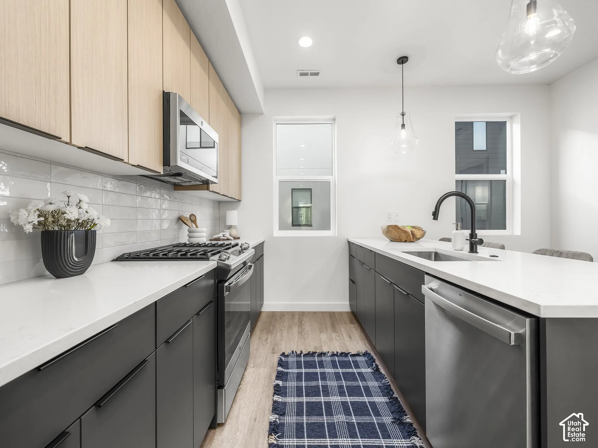 Modern kitchen featuring two-tone cabinetry with light wood-finish upper cabinets and dark lower cabinets, white countertops, and a subway tile backsplash