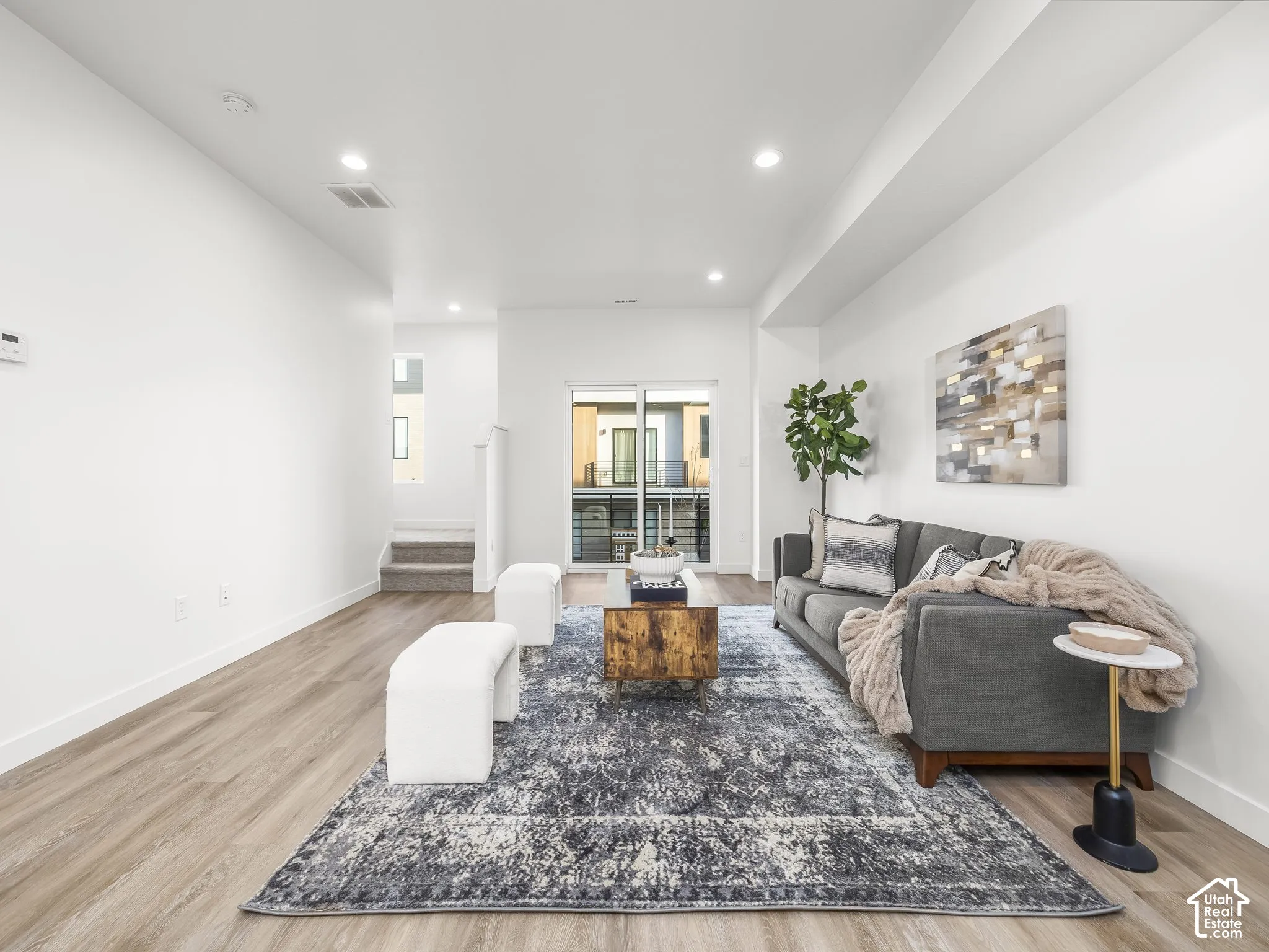 Spacious open-concept living area featuring light wood-finish flooring, recessed lighting, and a large sliding glass door