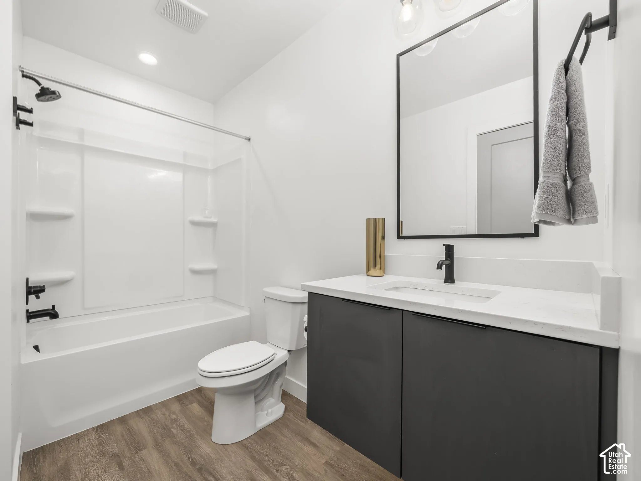 Bathroom featuring a white tub/shower combination with matte black fixtures, a contemporary vanity with a white countertop and rectangular undermount sink, matte black faucet, and wood-finish flooring
