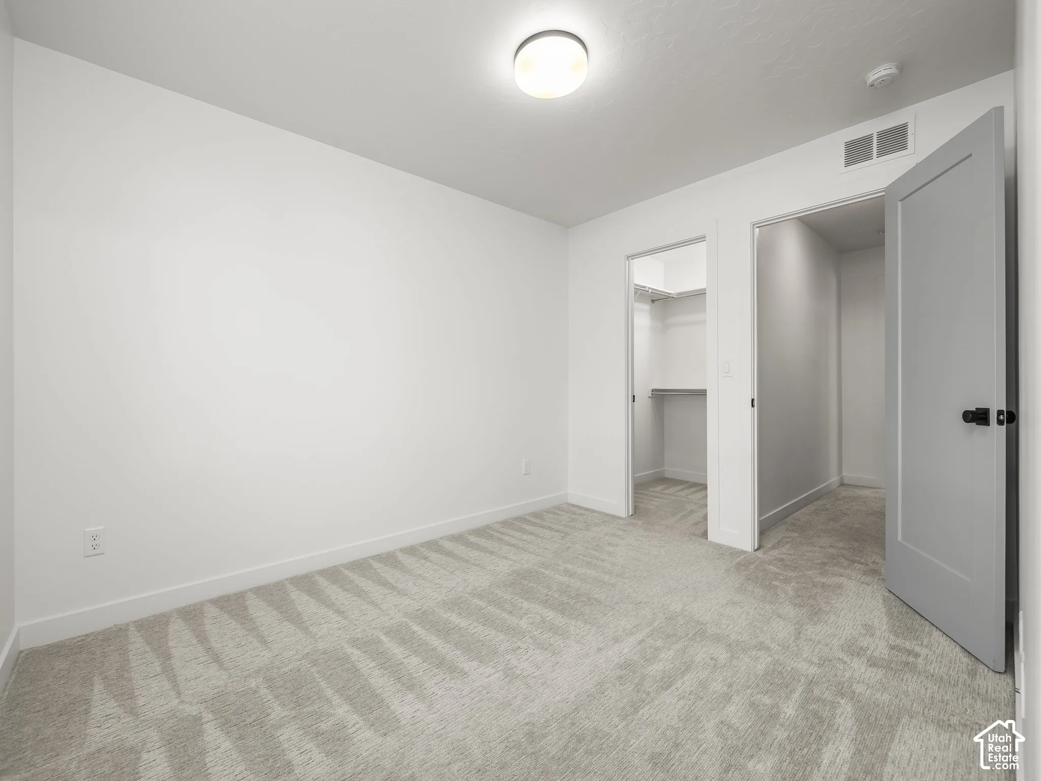 Neutral tone walls and carpeting throughout, featuring a walk-in closet with built-in shelving, a second closet, and a flush mount ceiling light fixture