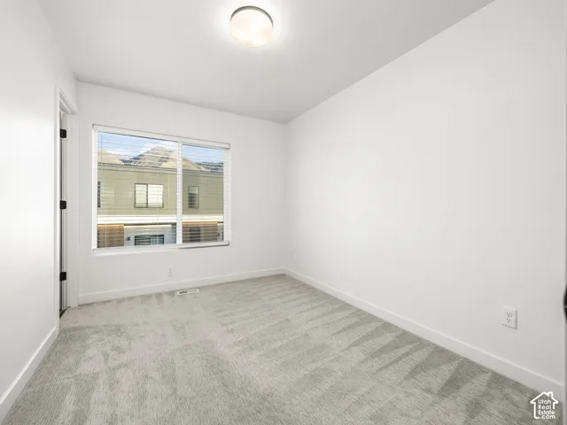 Bright interior room featuring a large window with horizontal blinds, light gray carpeting, and a flush-mount ceiling light