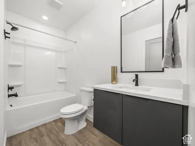 Bathroom featuring a white tub/shower combination with matte black fixtures, a contemporary vanity with a white countertop and rectangular undermount sink, matte black faucet, and wood-finish flooring