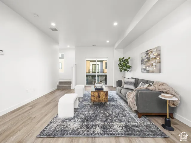 Spacious open-concept living area featuring light wood-finish flooring, recessed lighting, and a large sliding glass door