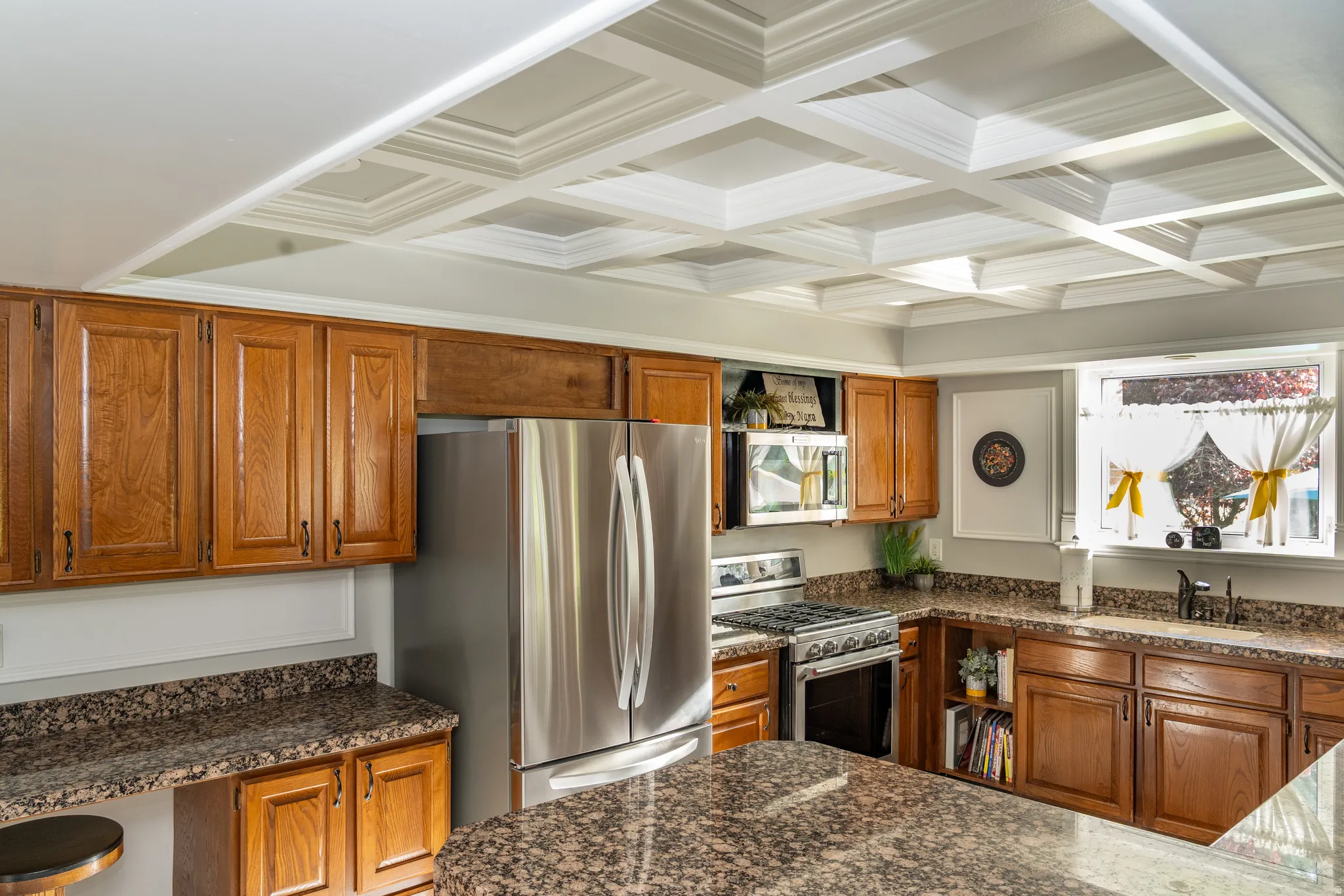 Kitchen featuring a coffered ceiling, wood cabinetry, granite countertops, and stainless steel appliances including a refrigerator, range, and microwave