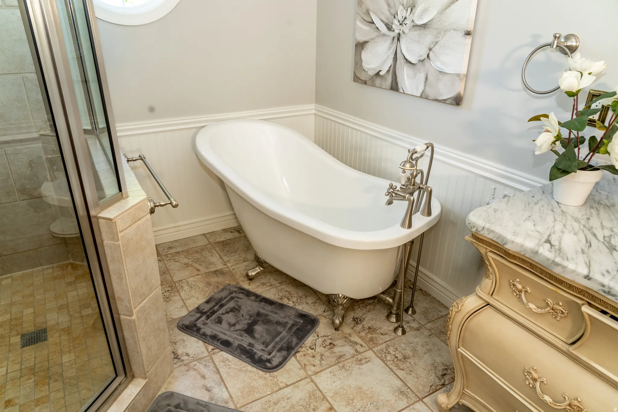 Bathroom featuring a freestanding clawfoot tub with a polished nickel faucet, full glass shower enclosure, vanity with a patterned stone countertop, tile flooring, and wainscoting