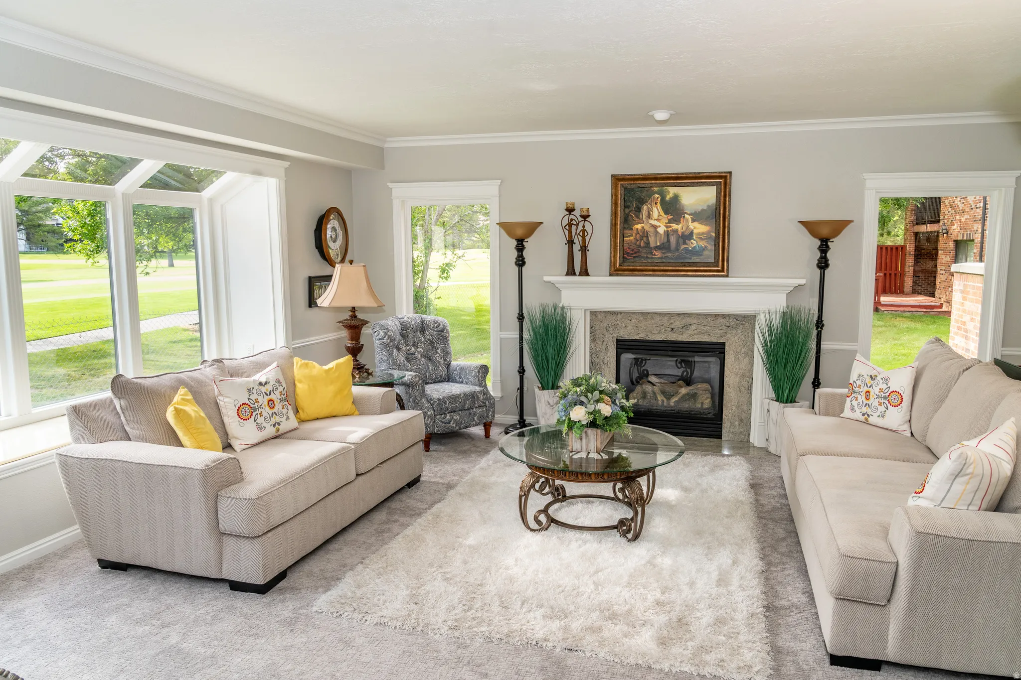 Living area featuring a stone-clad fireplace with a white mantel, large bay windows, light-toned carpeting, and crown molding