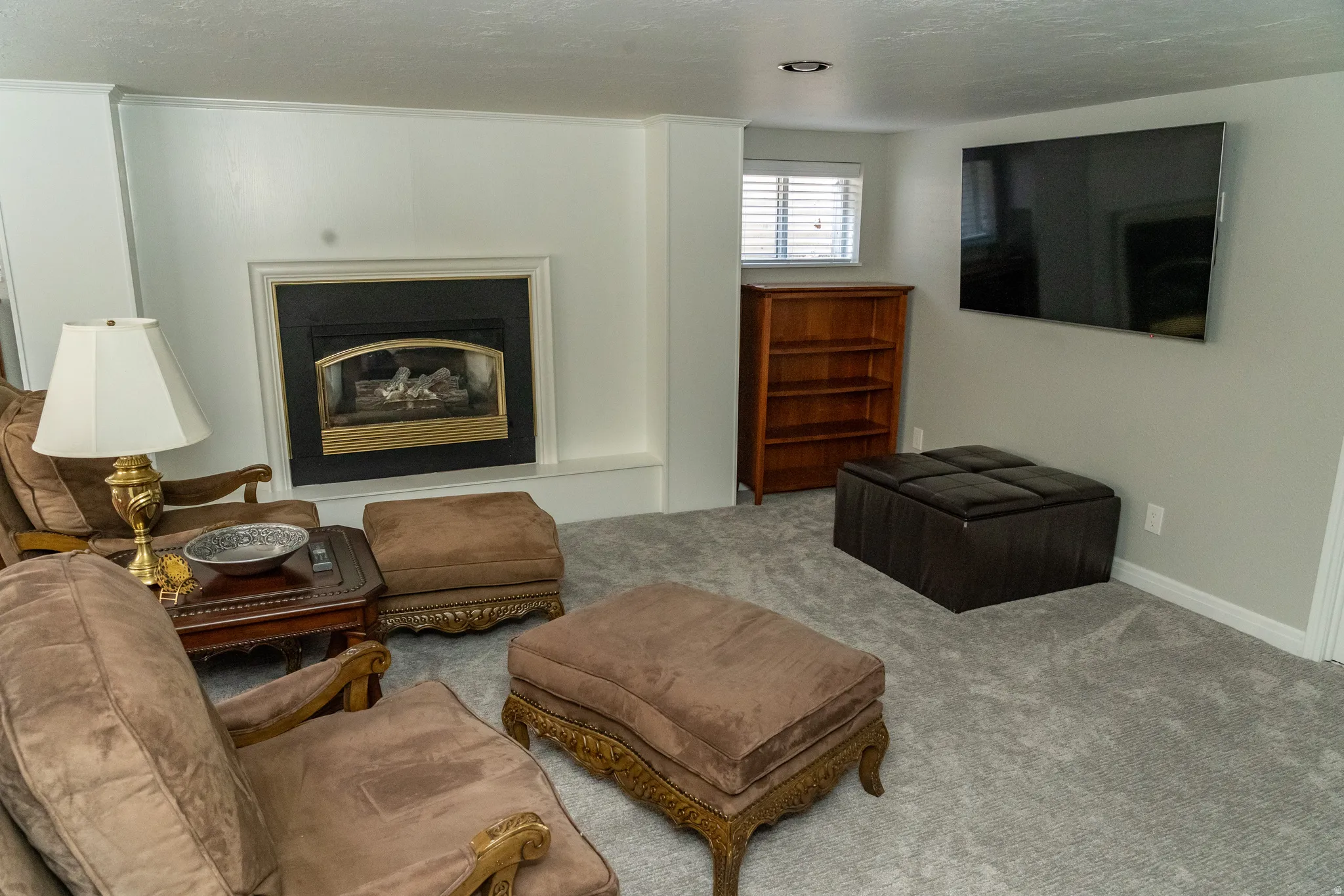 Recessed lighting illuminating a spacious room with a prominent fireplace featuring a black insert and gold-tone trim