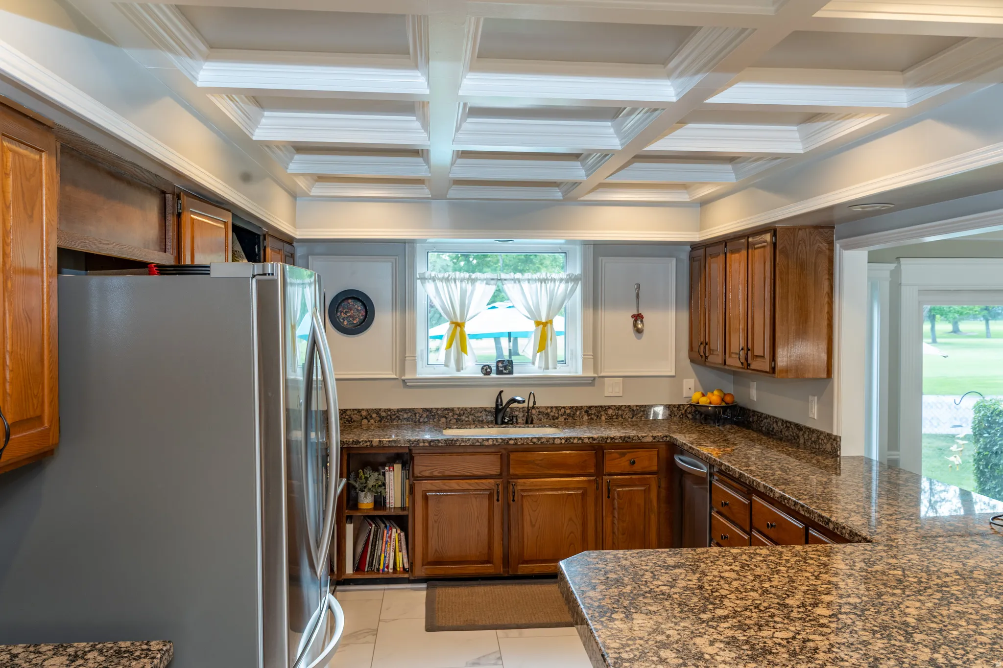 Kitchen featuring a coffered ceiling, wood cabinetry, stone countertops, and a built-in stainless steel dishwasher