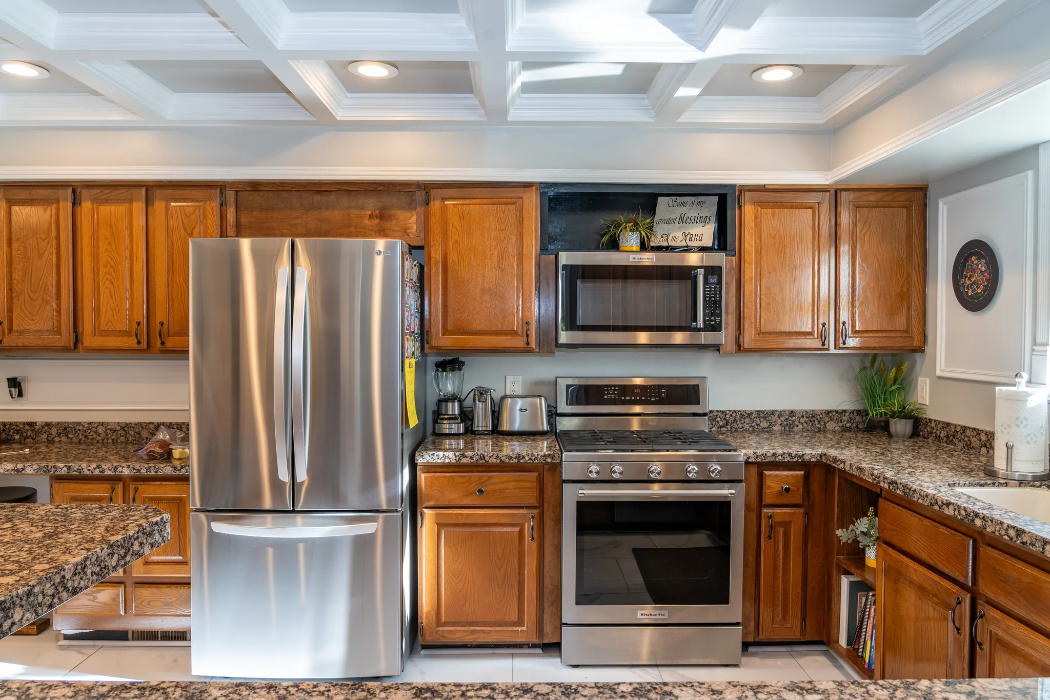 Kitchen featuring a coffered ceiling with recessed lighting, wood cabinetry, granite countertops, and stainless steel appliances