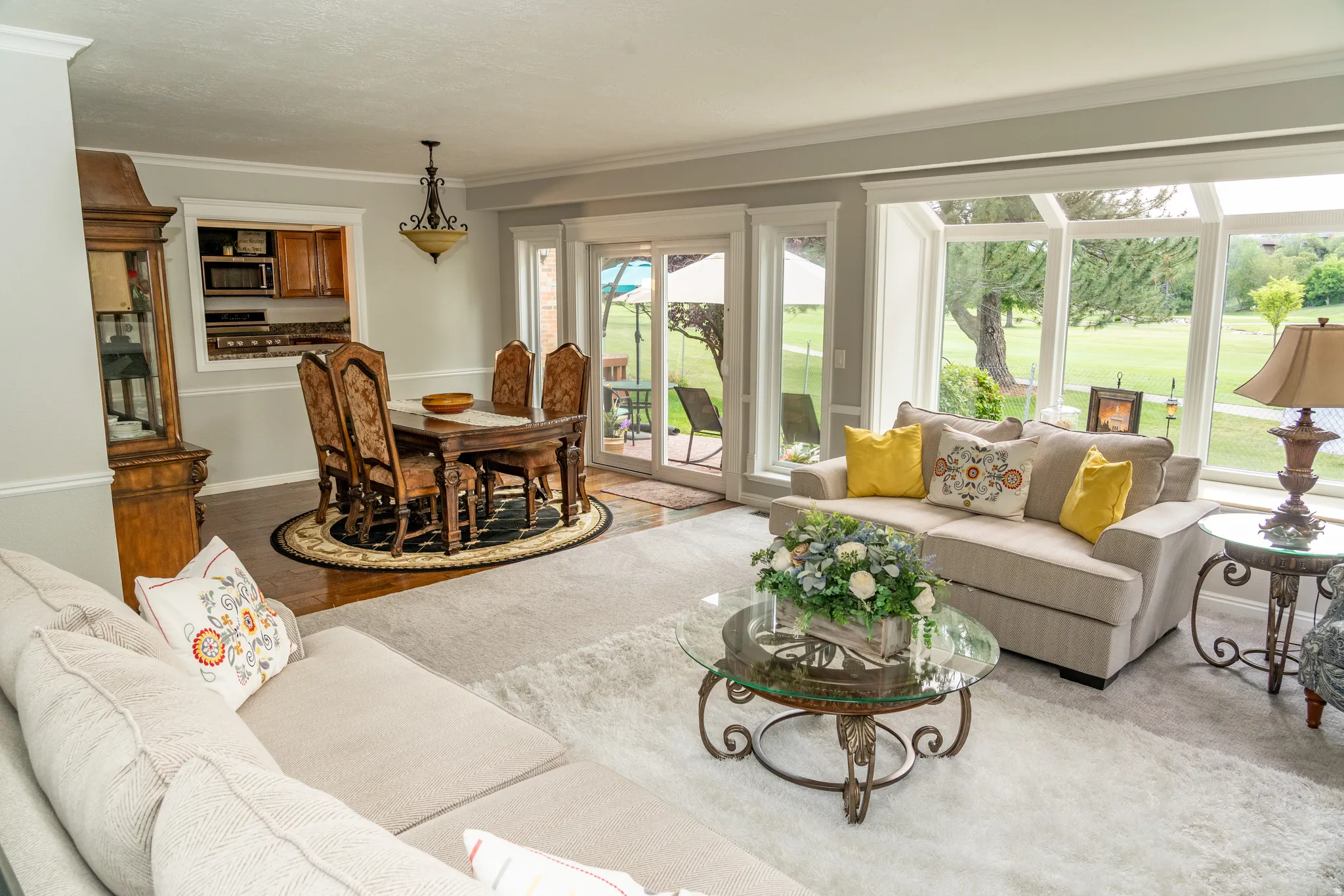 Bright living area featuring expansive windows, a sliding glass door, a pass-through opening to the kitchen, crown molding, and wood-finish flooring in the dining area