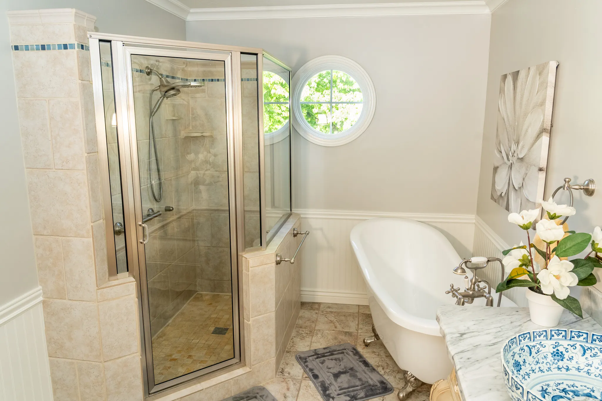Bathroom featuring a glass-enclosed shower with tile surround, a freestanding clawfoot tub, a circular accent window, crown molding, and wainscoting