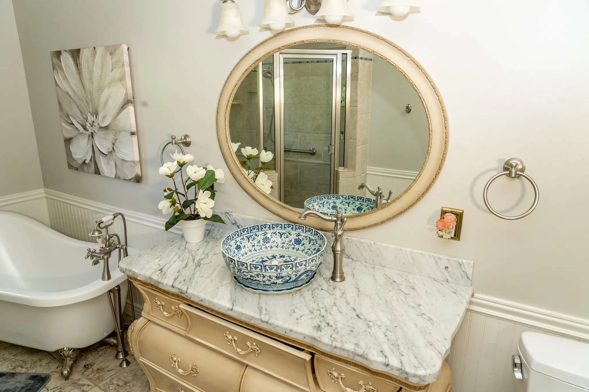 Bathroom featuring a clawfoot tub, beadboard wainscoting, an ornate vanity with a stone countertop, a vessel sink, and an oval mirror