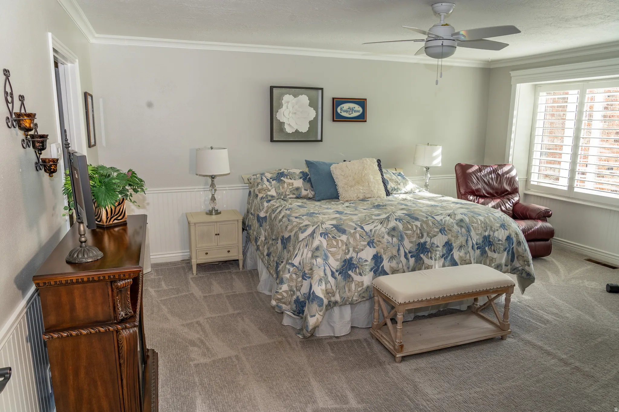 Room featuring crown molding, white wainscoting, light gray carpeting, a ceiling fan, and window shutters