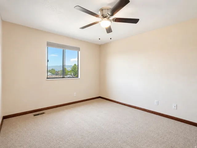 Carpeted room featuring a ceiling fan with integrated lighting, a large window offering mountain and sky scenery, and dark wood trim