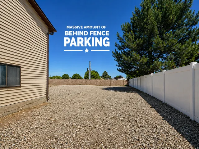 Expansive gravel parking area bordered by a white vinyl fence and a mature tree